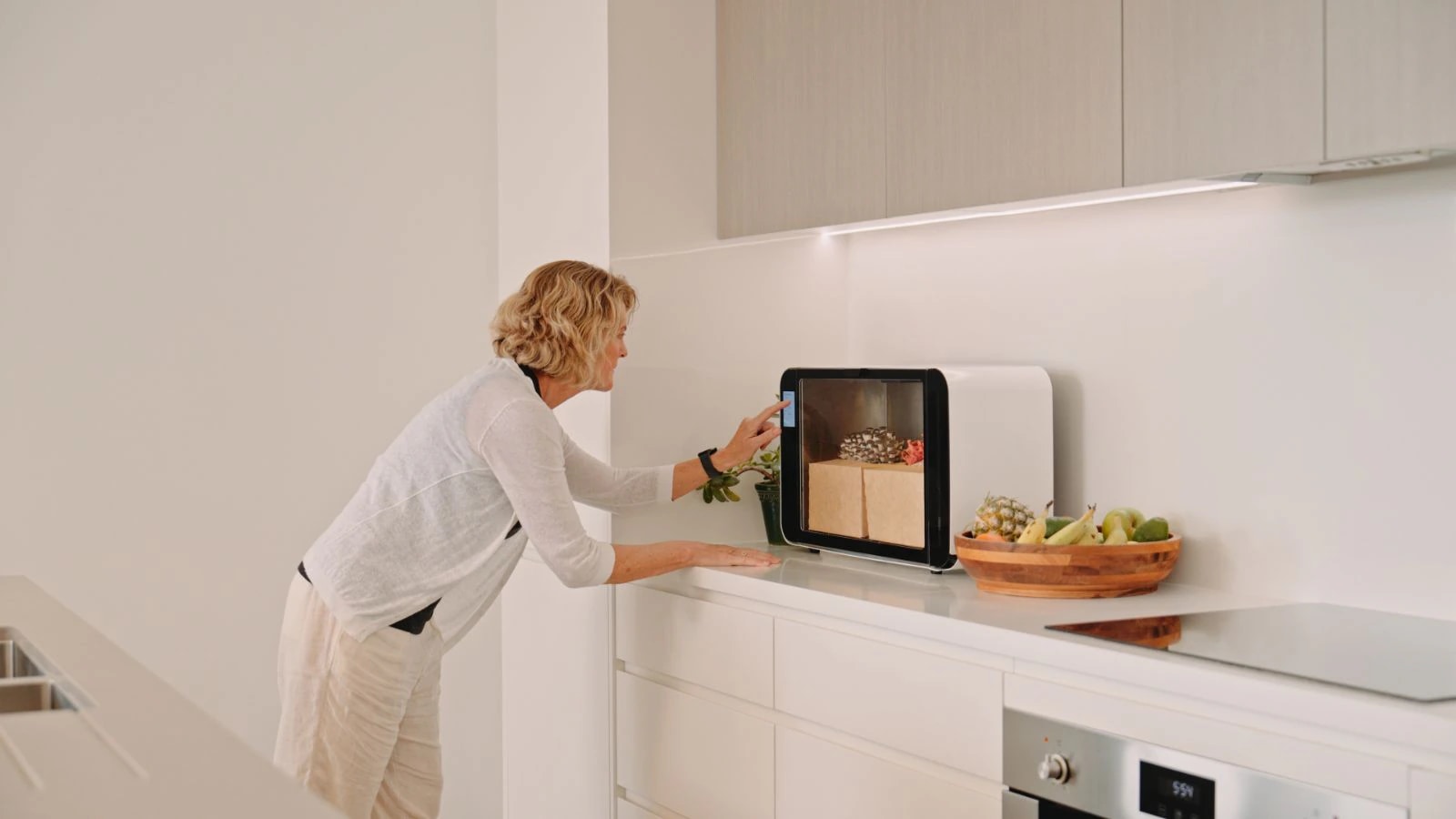 A woman using the Flush cabinet's touchscreen on her kitchen bench, oyster mushrooms growing inside
