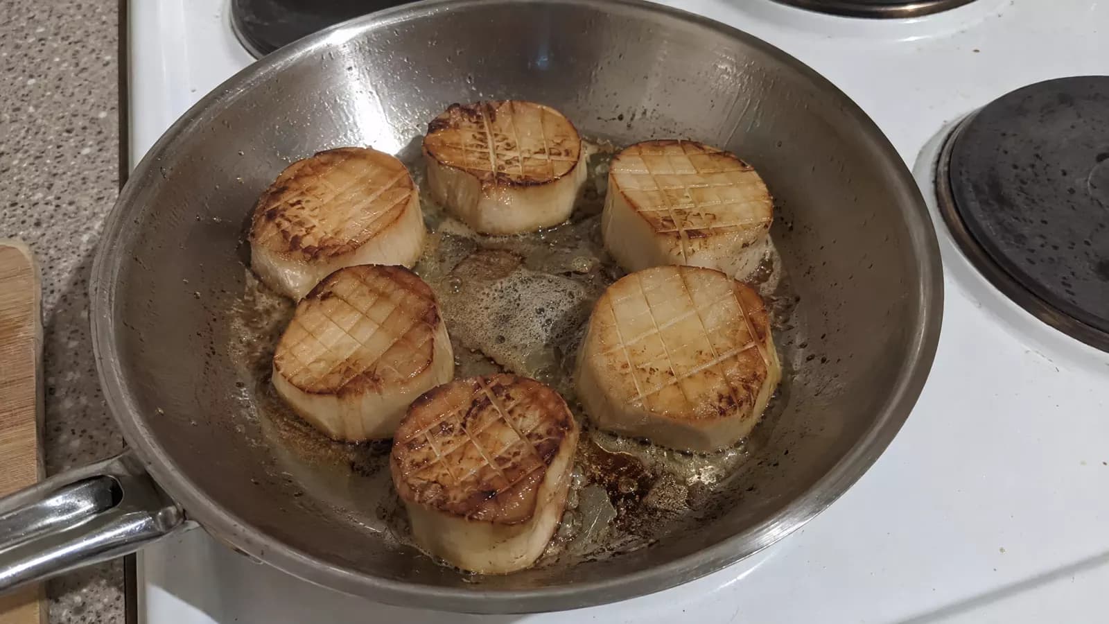 Scored rounds of king oyster mushroom stem browning in butter in a frying pan
