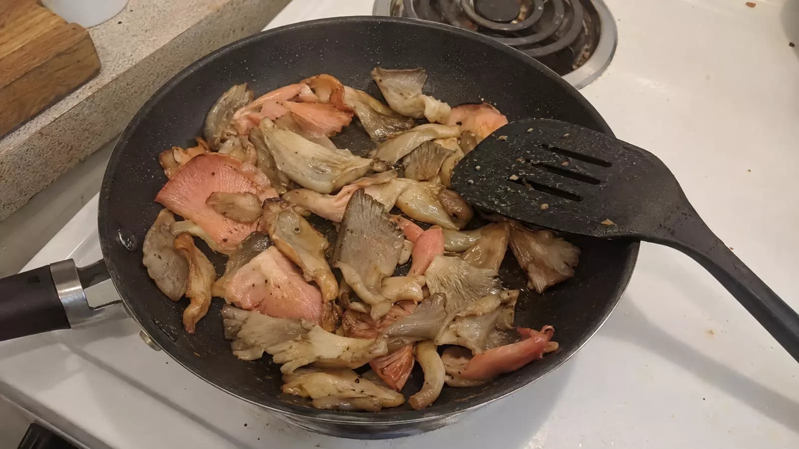 Grey and pink oyster mushrooms frying in a pan on a home stovetop