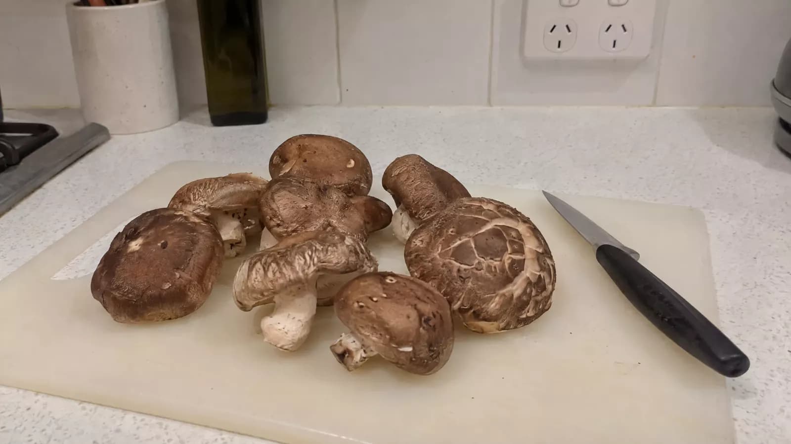 Fresh shiitake mushrooms on a chopping board next to a kitchen knife in a home kitchen