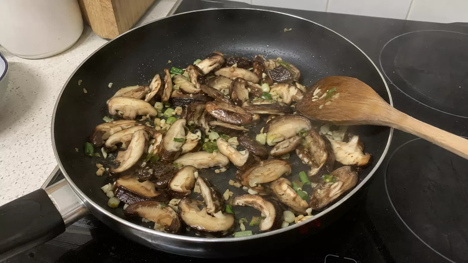 Sliced shiitake mushrooms stir-frying with garlic and spring onion in a frying pan